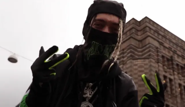 STONAN masqué en tenue noire, gants fluo, image extraite d'un clip